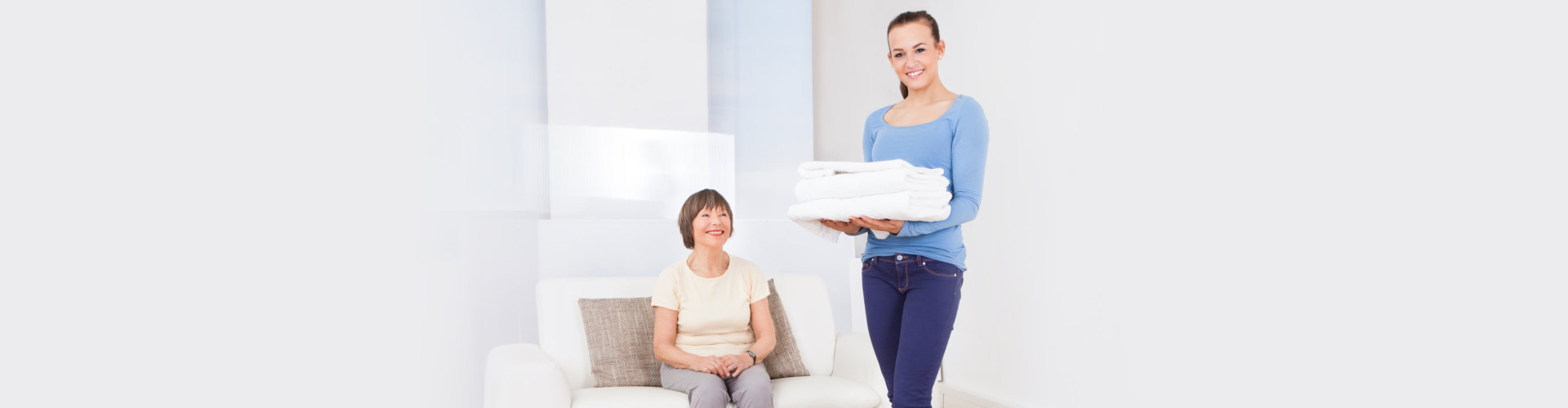 Caretaker carrying stack of folded towels with senior woman